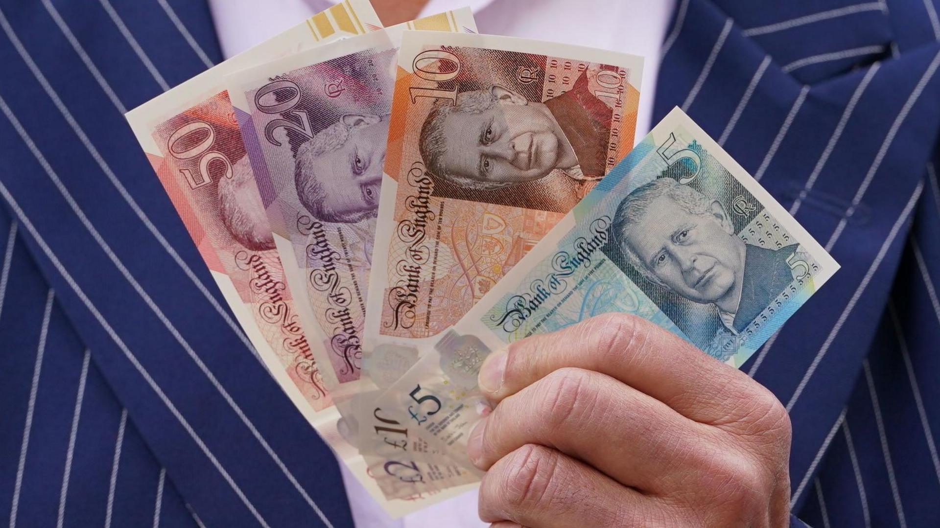 Man in a pinstripe suit holding UK money - cash notes of £50, £20, £10 and £5